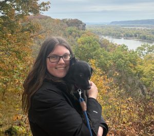 Megan Guyer holding her dog with lush greenery in the background.